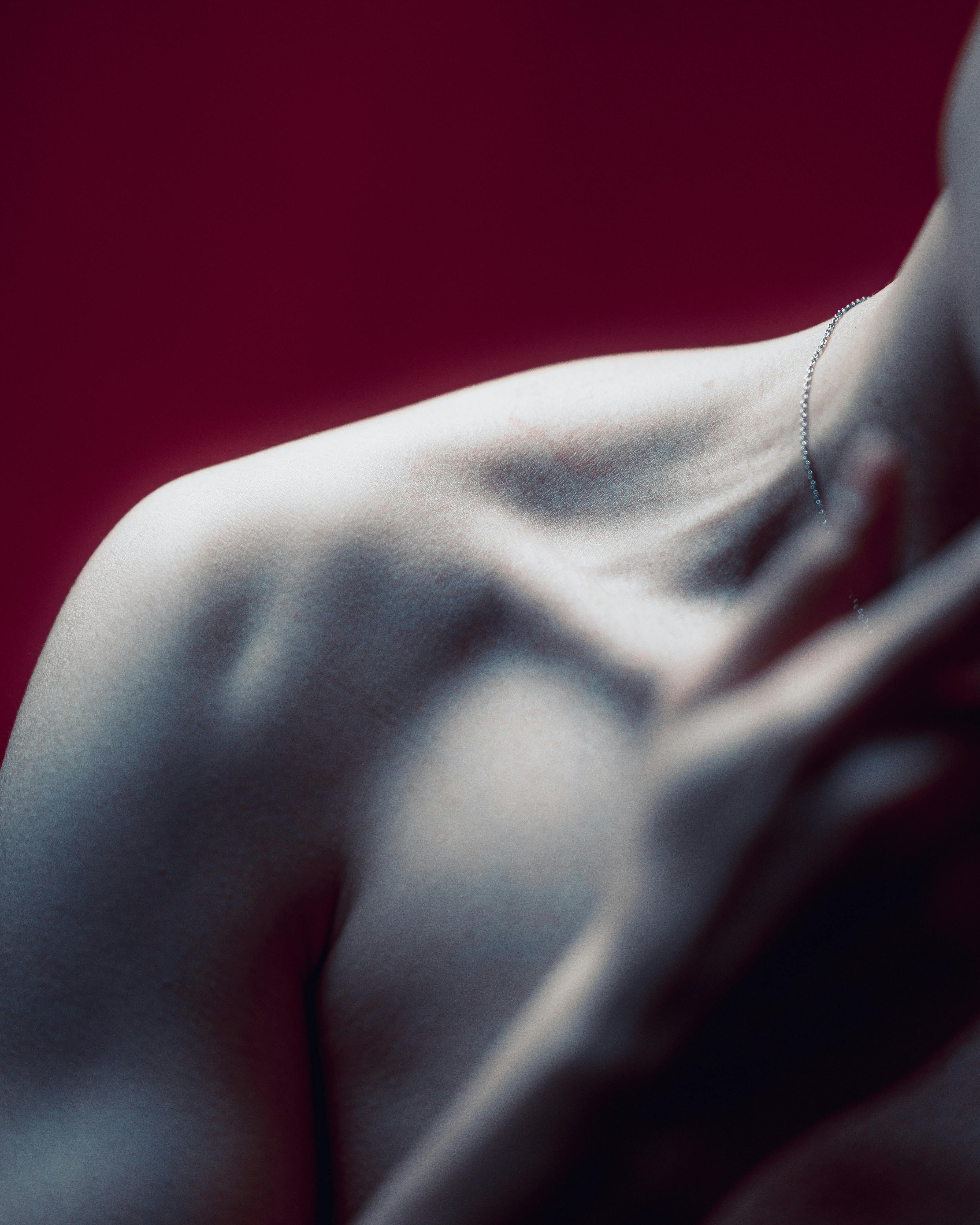 Close-up of a shoulder and neck area with soft lighting and a dark red background.
